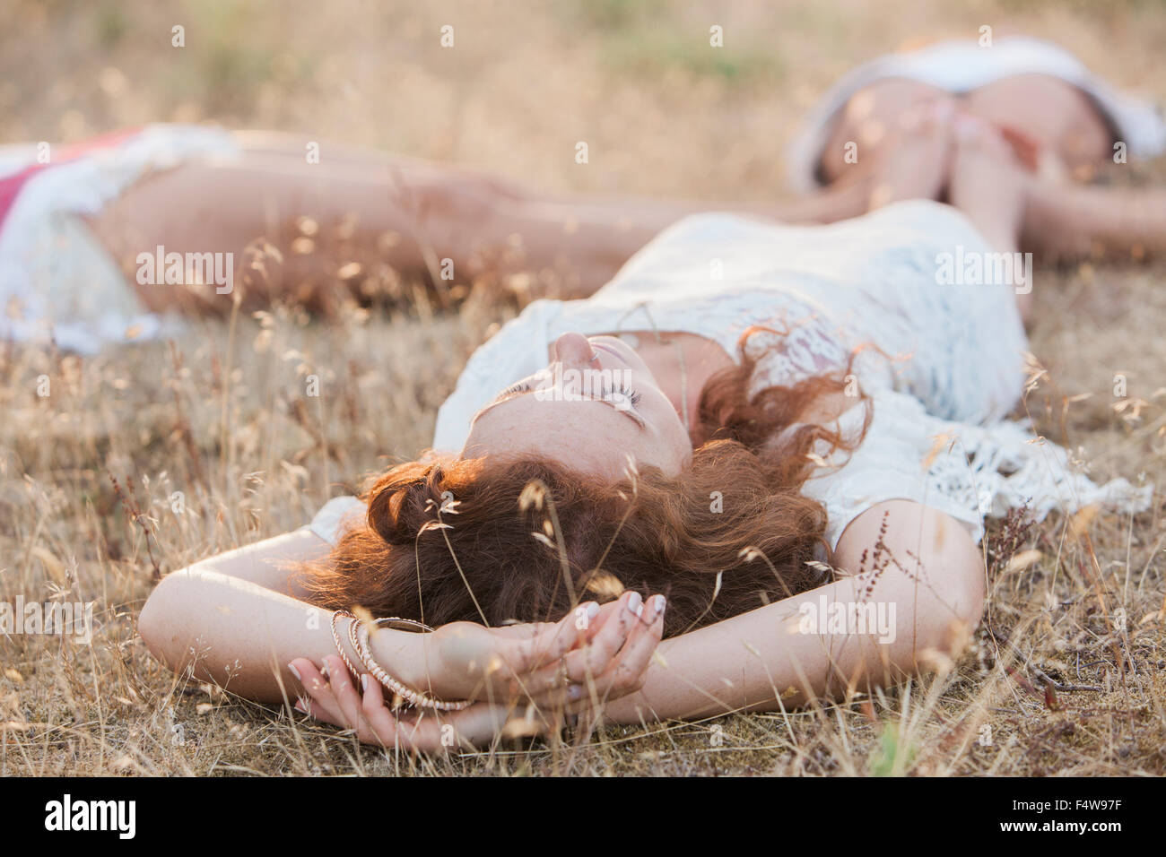 Boho women laying in circle with feet touching in rural field Stock Photo