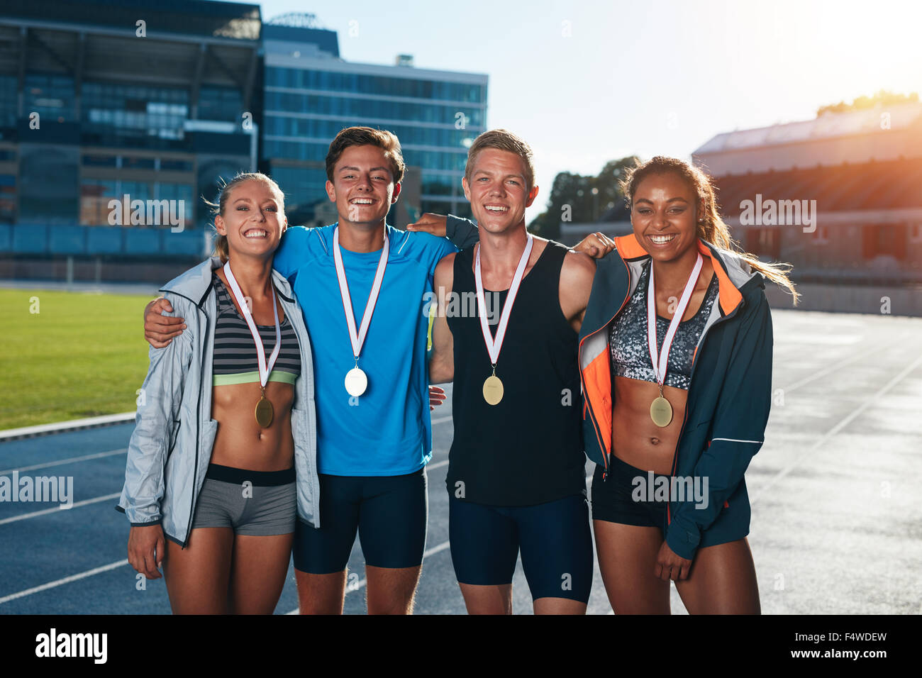 Group of athletes with medals .Two young woman and man together looking at camera and smiling while standing on athletics race t Stock Photo