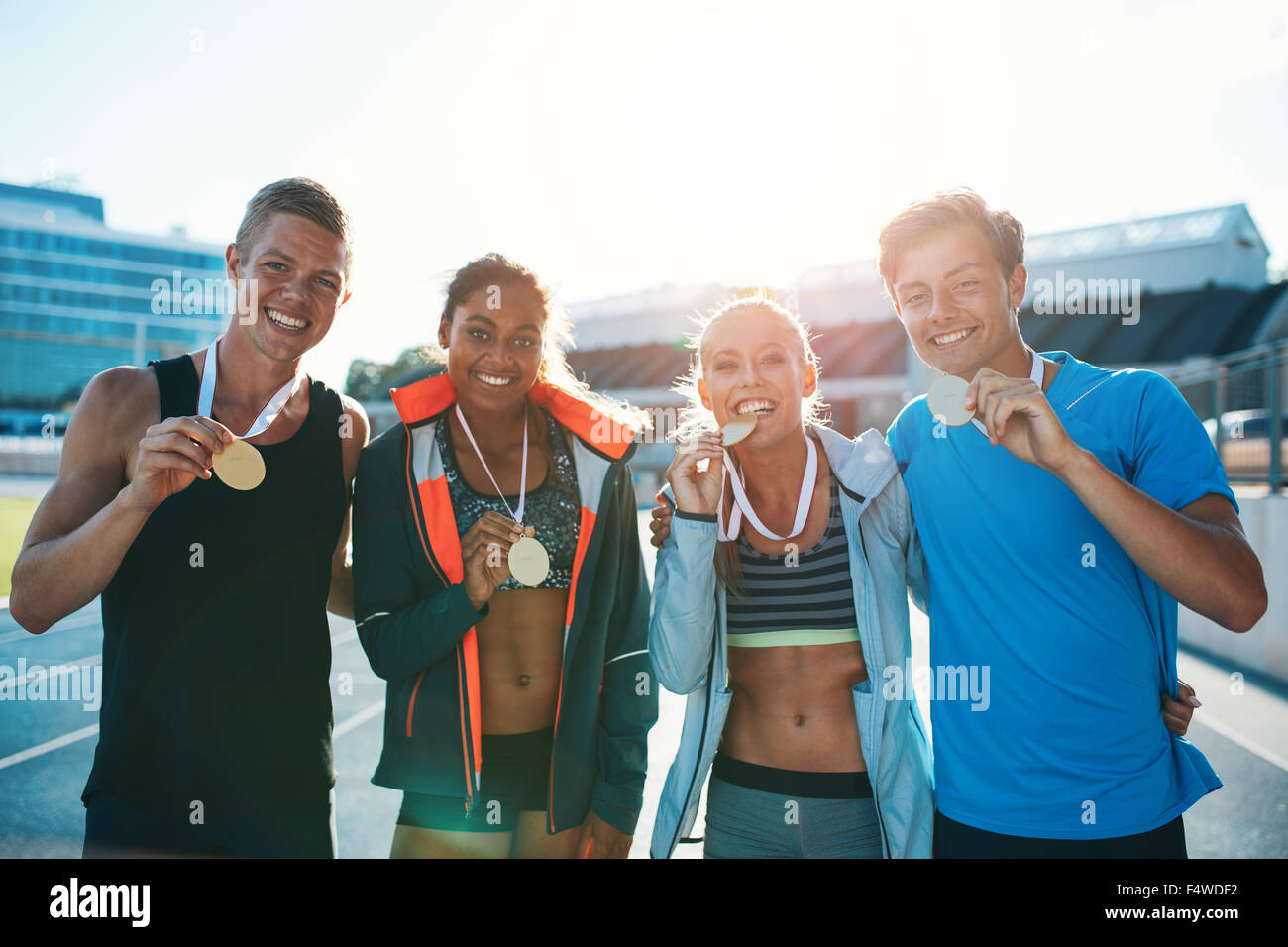 Portrait of ecstatic young runners showing medals. Young men and women looking excited after winner a running race. Team of mult Stock Photo