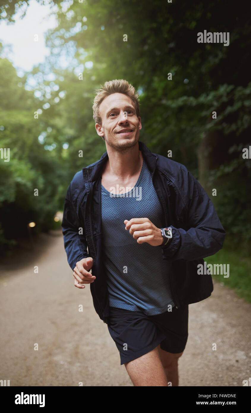 Healthy young man jogging through a park on a sunny morning doing his daily training and workout, close up view approaching the Stock Photo