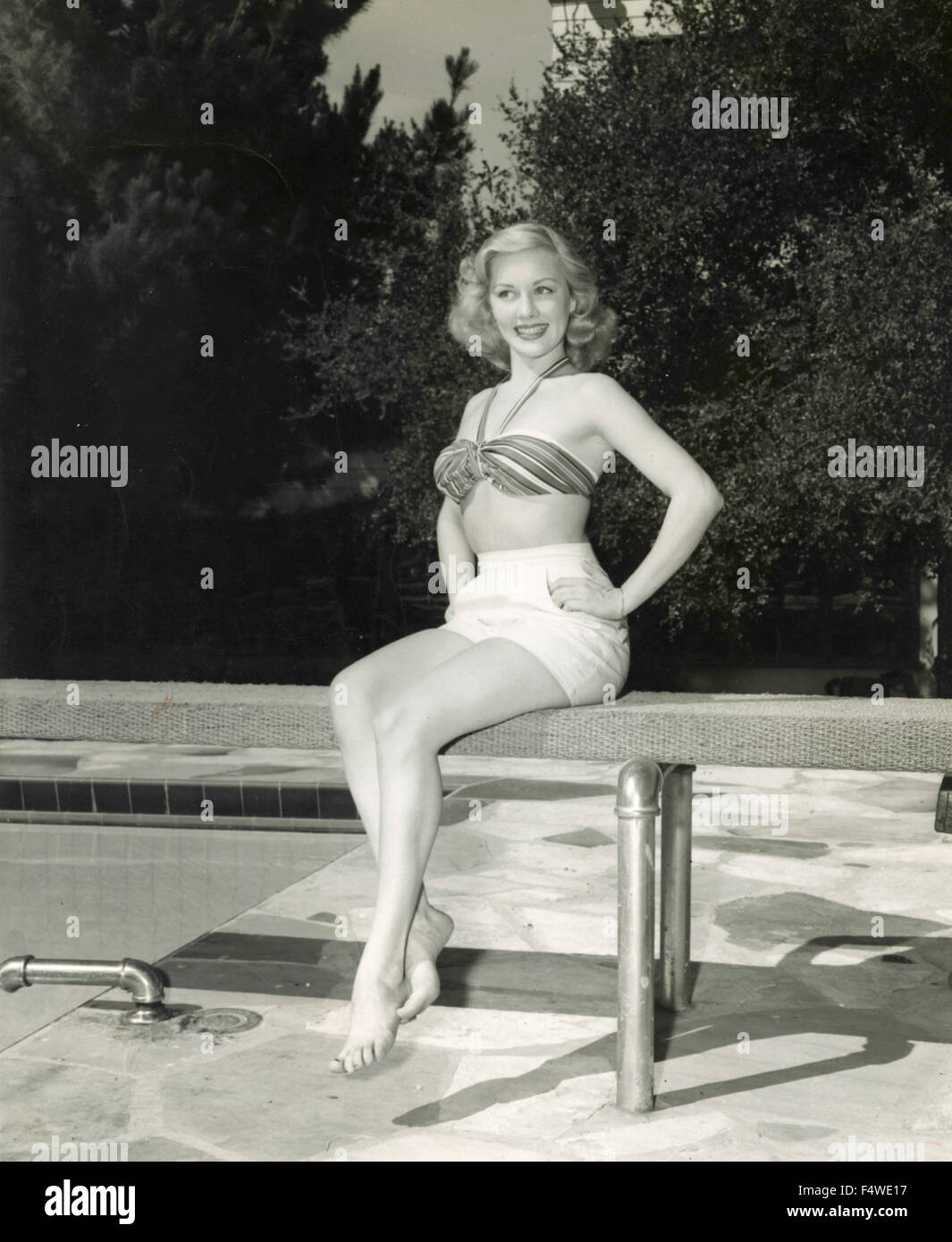 The American actress Lila Leeds with a two piece swimsuit sitting on the trampoline at a swimming pool Stock Photo