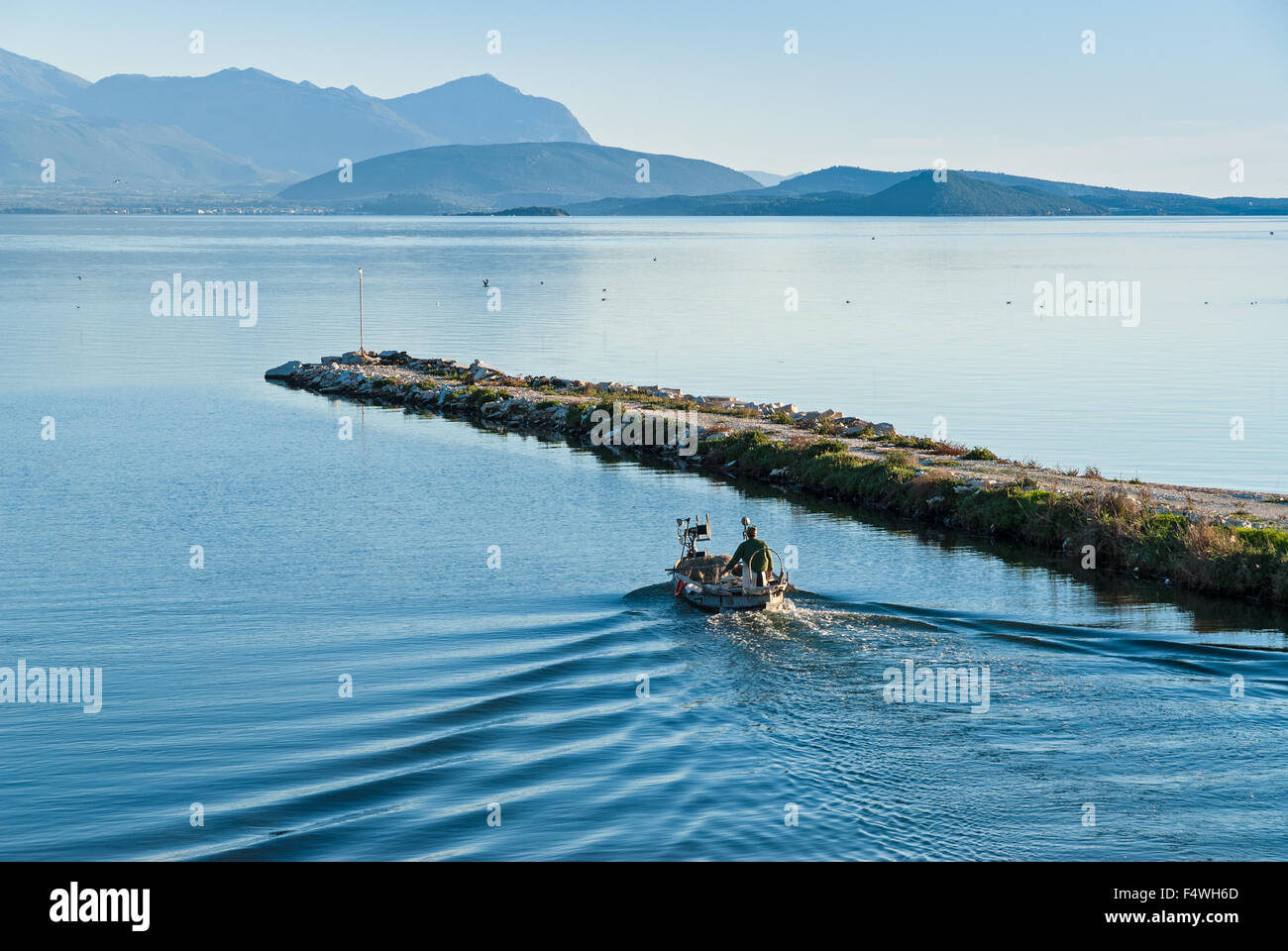 A fisherman in his traditional wooden boat leaves the harbor, going to work on November 10, 2013 in Amvrakikos gulf, Greece. Stock Photo