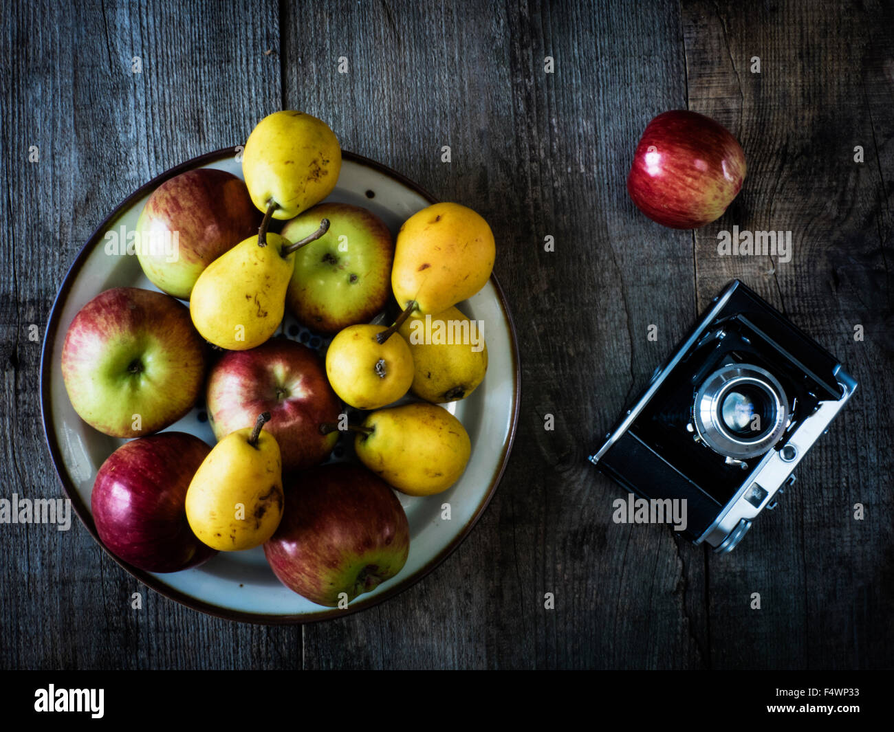 antique photo camera, pears and apples on wooden weathering background Stock Photo
