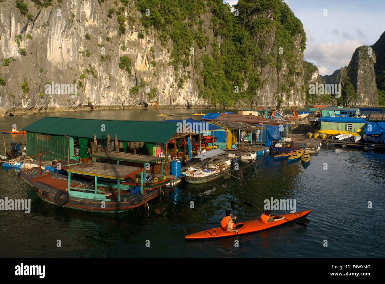 Kayaking past a floating fishing village in Halong Bay. Fish farm village amongst karst limestone mountains at Cat Ba National Park, Ha long,Halong Bay, Ha long,Halong Bay, Vietnam. Stock Photo