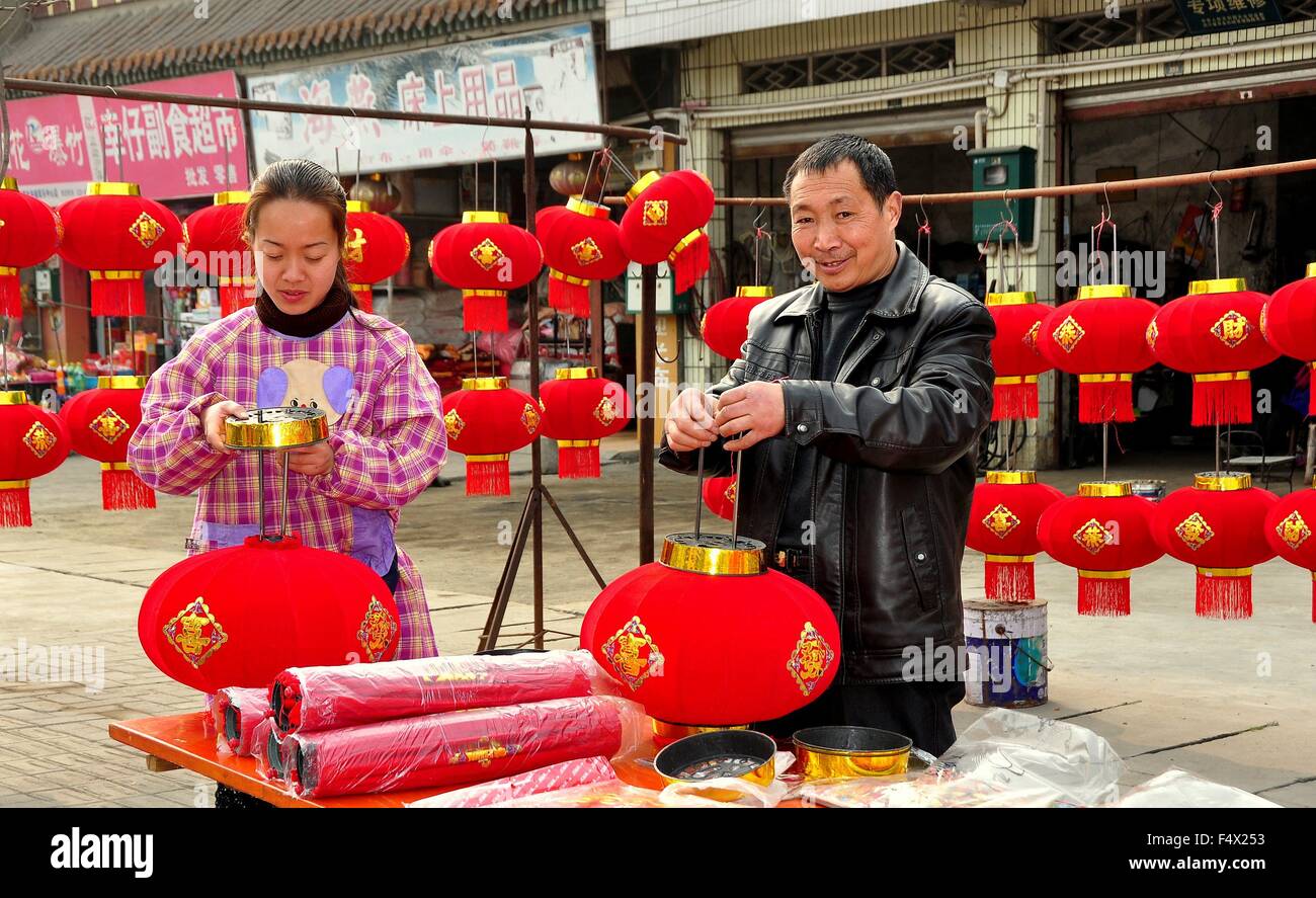 Jun Le, China  Husband and wife preparing to display red fabric Chinese New Year lanterns at their roadside stand Stock Photo