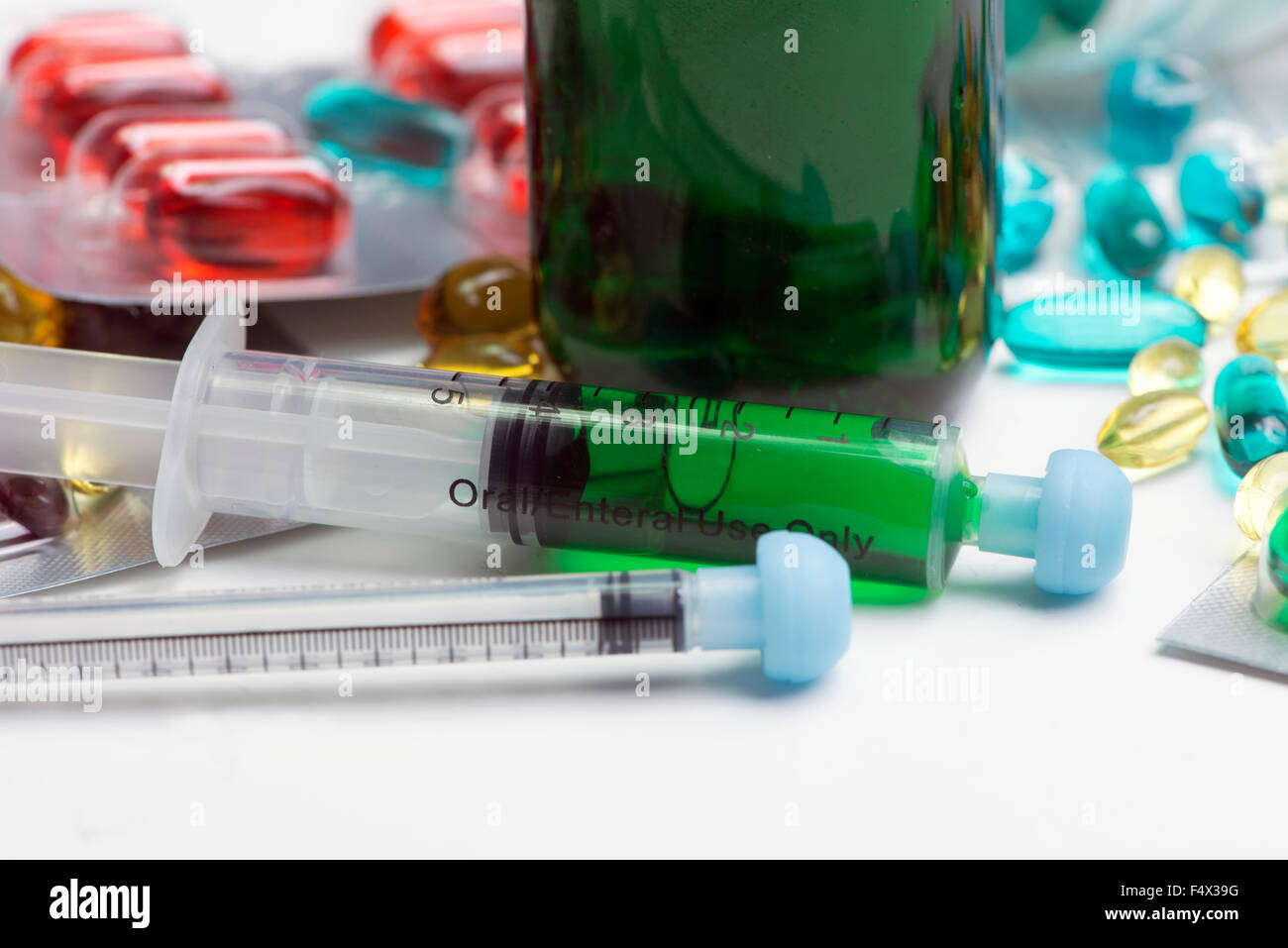 Close-up of green cough medicine bottle with oral syringes and cold remedy capsules. Stock Photo