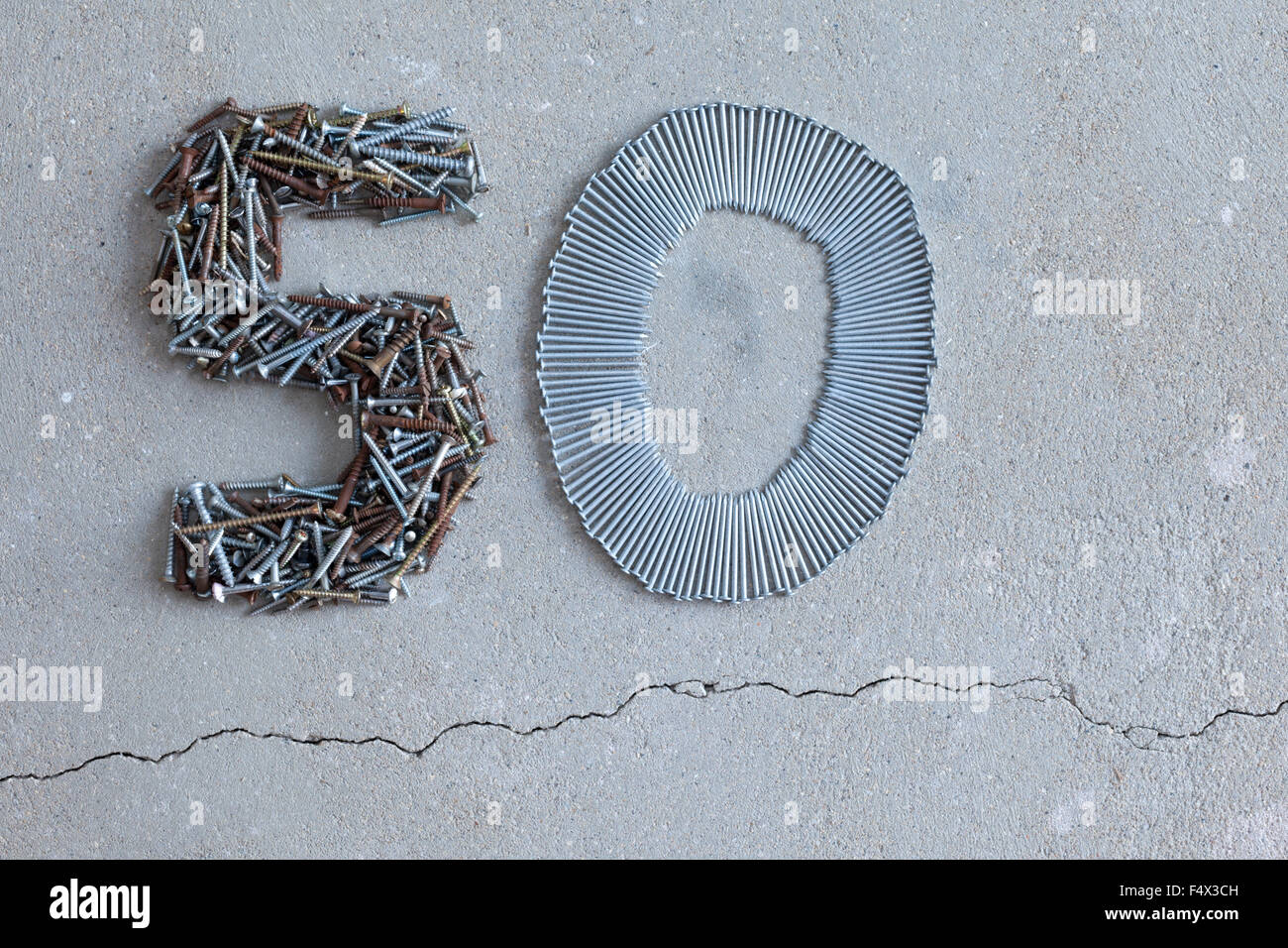 50 fifty number arranged out of old screws and nails on a concrete floor Stock Photo