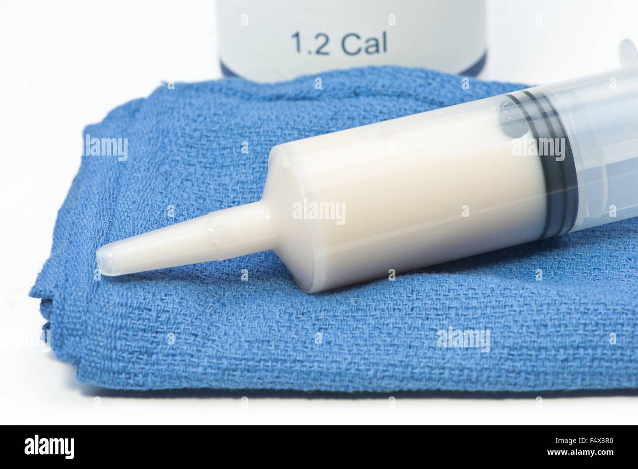 Close up view of feeding syringe with can of enteral formula and towel