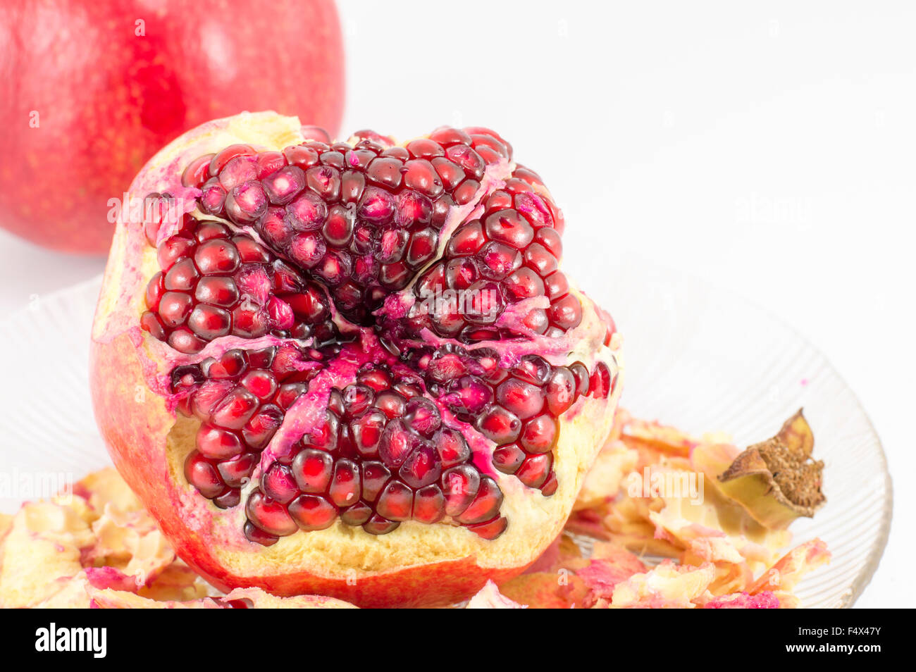 Juicy pomegranate partially peeled on a plate on white background Stock Photo