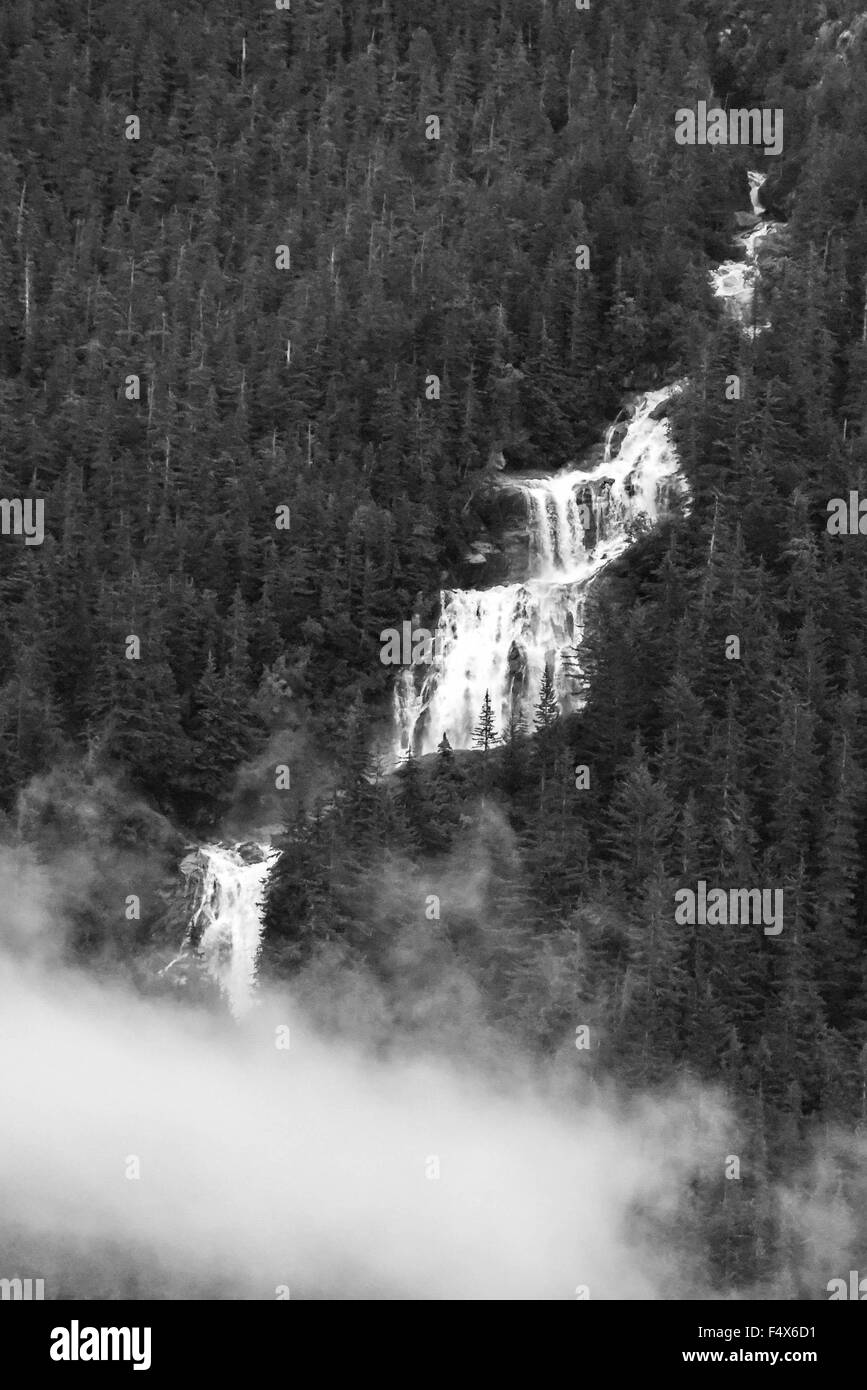 A scenic mountainside waterfall crashes down the cliff face through the clouds near Skagway Alaska | Lynn Canal fjord cruise - inside passage Stock Photo