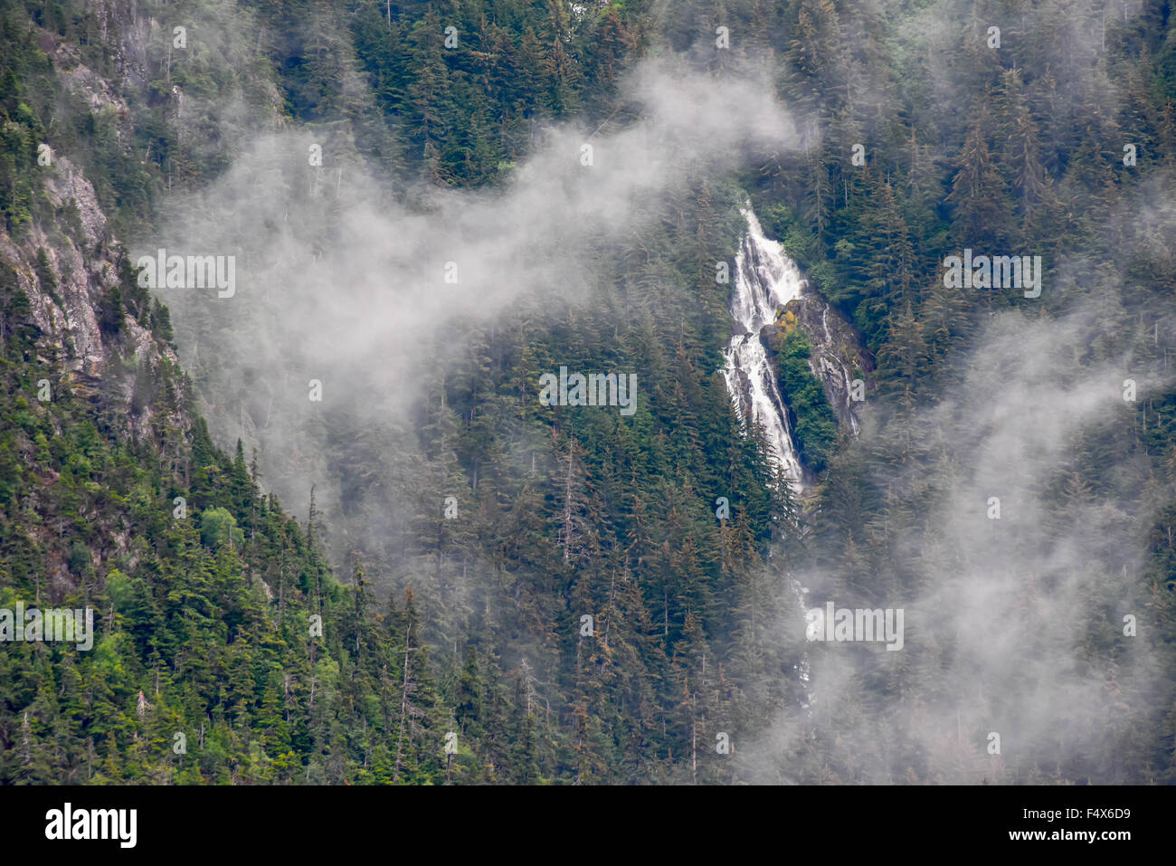A scenic mountainside waterfall crashes down the cliff face through the clouds near Skagway Alaska | Lynn Canal fjord cruise - inside passage Stock Photo