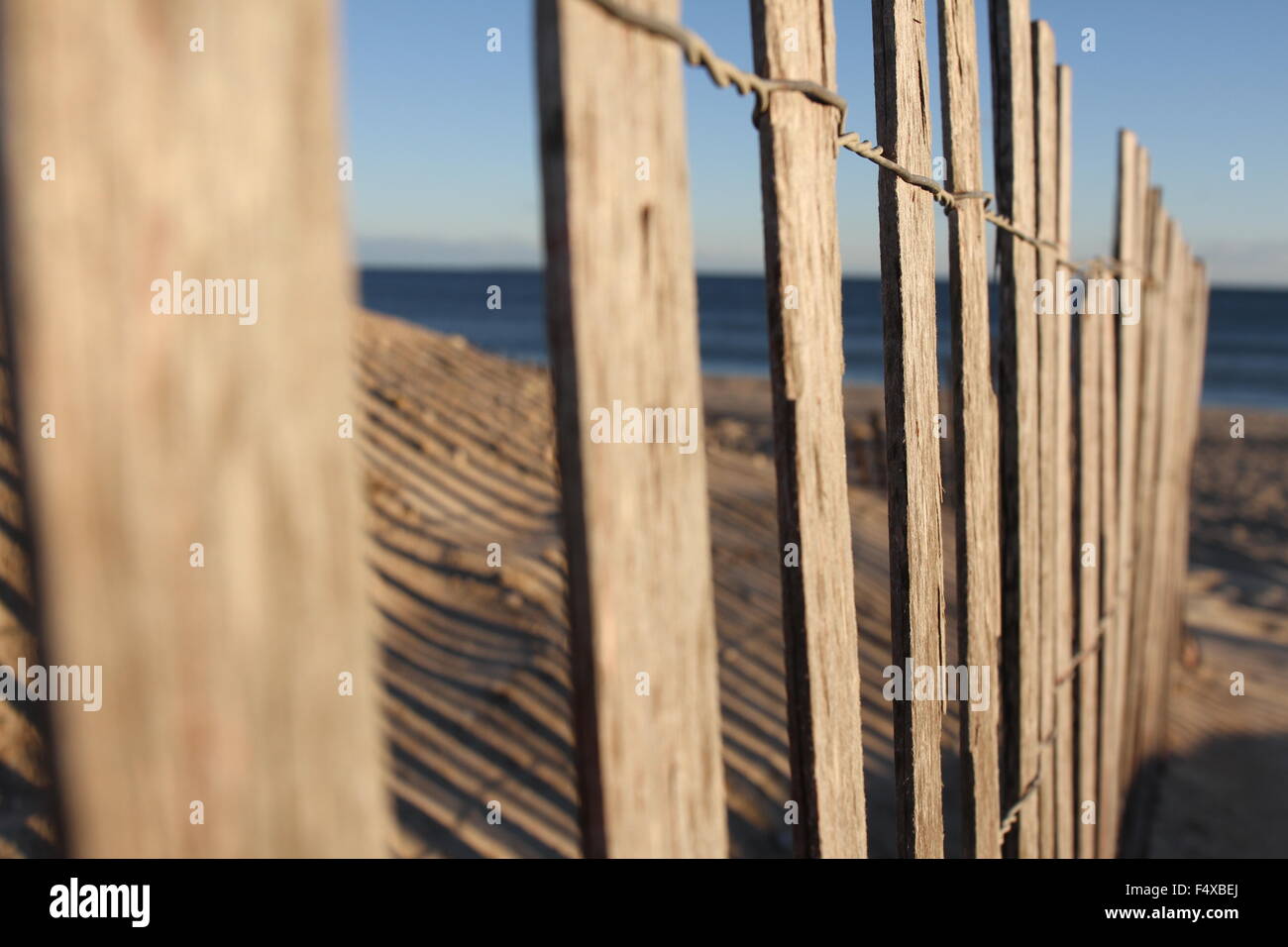 Old picket fence casting a shadow on a sandy beach at sunset. Stock Photo