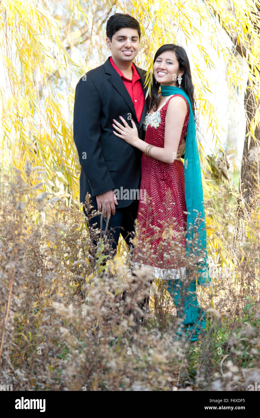 A happy and young Indian couple posing under a willow tree on a sunny ...