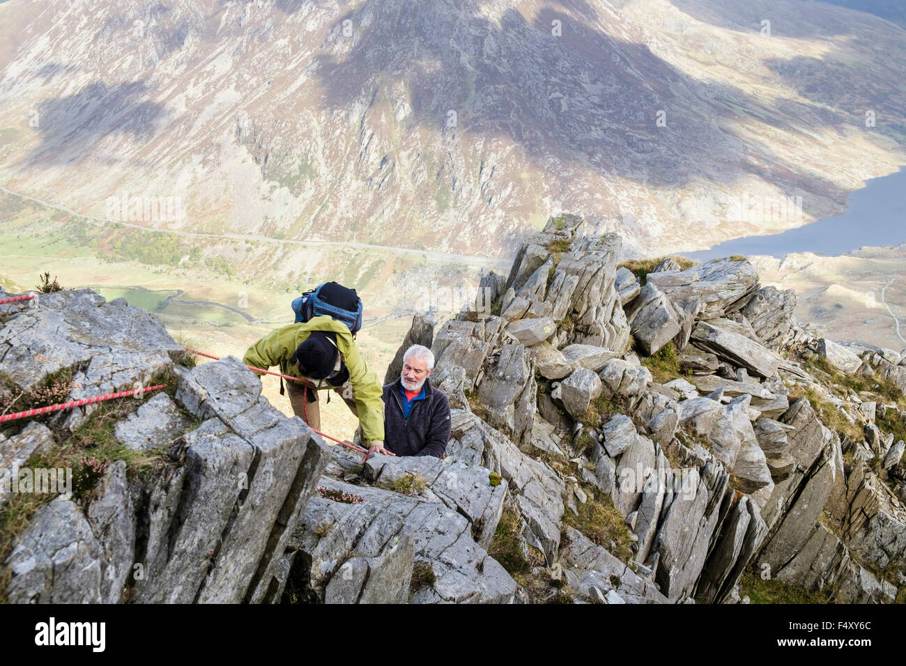 Active senior hikers climbing using a safety rope on Y Garn mountain north east ridge high above Ogwen Valley in mountains. Snowdonia (Eryri) Wales UK Stock Photo