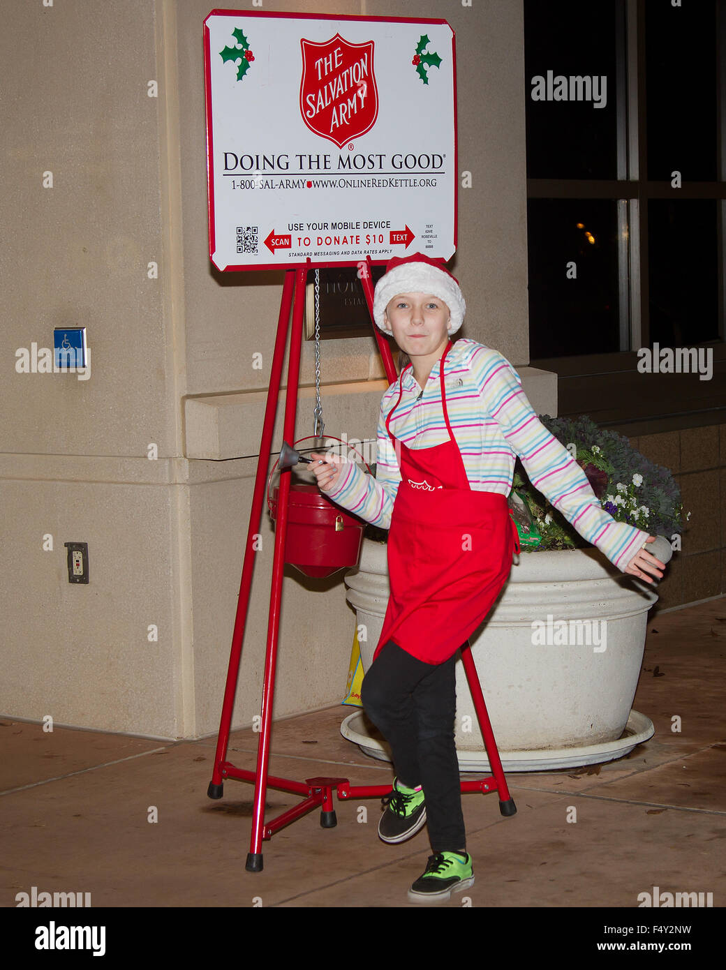 A Salvation Army volunteer dancing and doing handstands with her bell as she tries to collect donations. Stock Photo