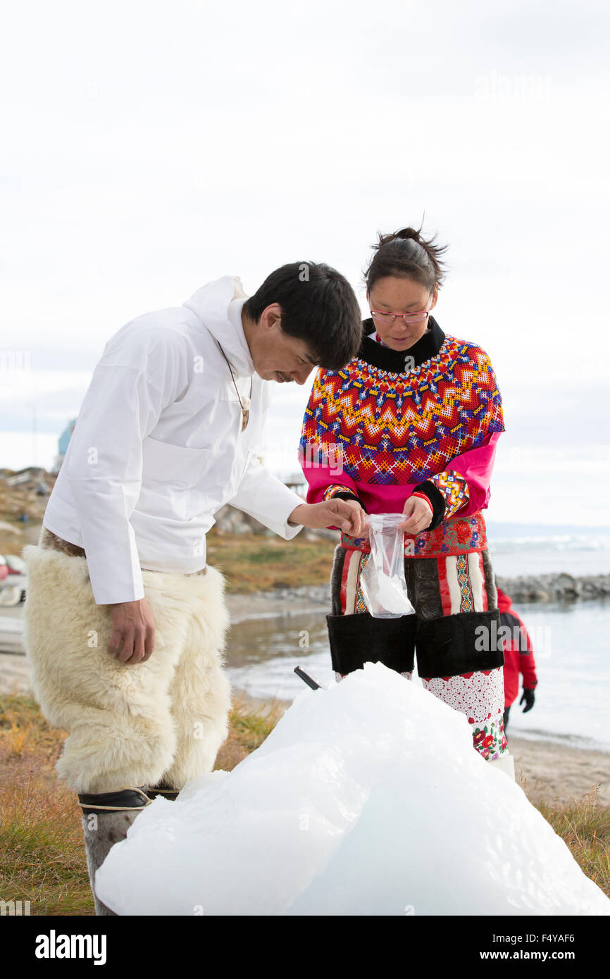 Greenland, Disko Bay, Saqqaq. Villagers in traditional attire chip fresh ice of a berg and bag to drink once melted. Stock Photo