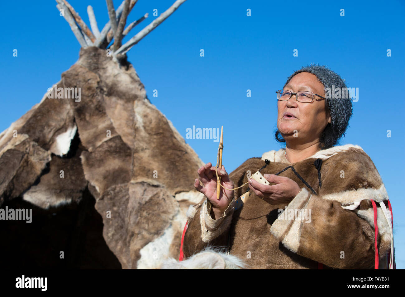 Canada, Nunavut, Hudson Bay, Kivalliq, Arviat, local woman demonstrates historic tools used by Inuit, polar tent in background. Stock Photo