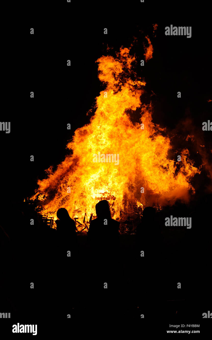 People are silhouetted against the flames of a large bonfire lit to celebrate  November the 5th, also known as Bonfire Night, in the village of Firle in East Sussex, England. Stock Photo
