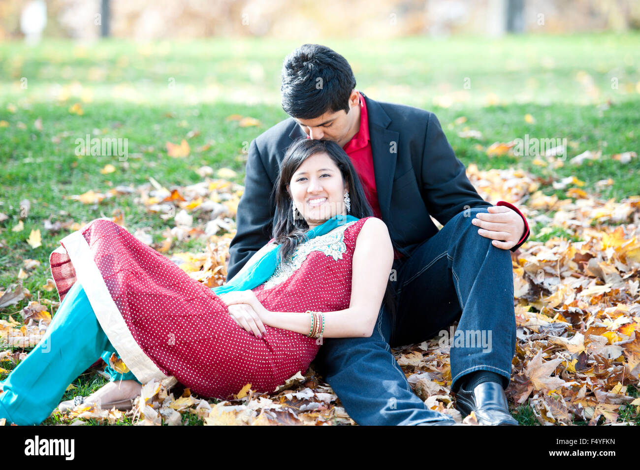 A young and happy Indian couple posing on a pile of leaves in the fall ...