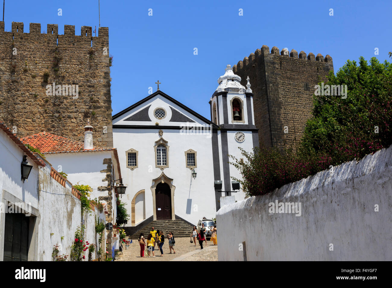 Tourist standing in front of the Igreja de Santiago (Church of Santiago) which is framed on either side by the old walls in Obidos, Portugal Stock Photo