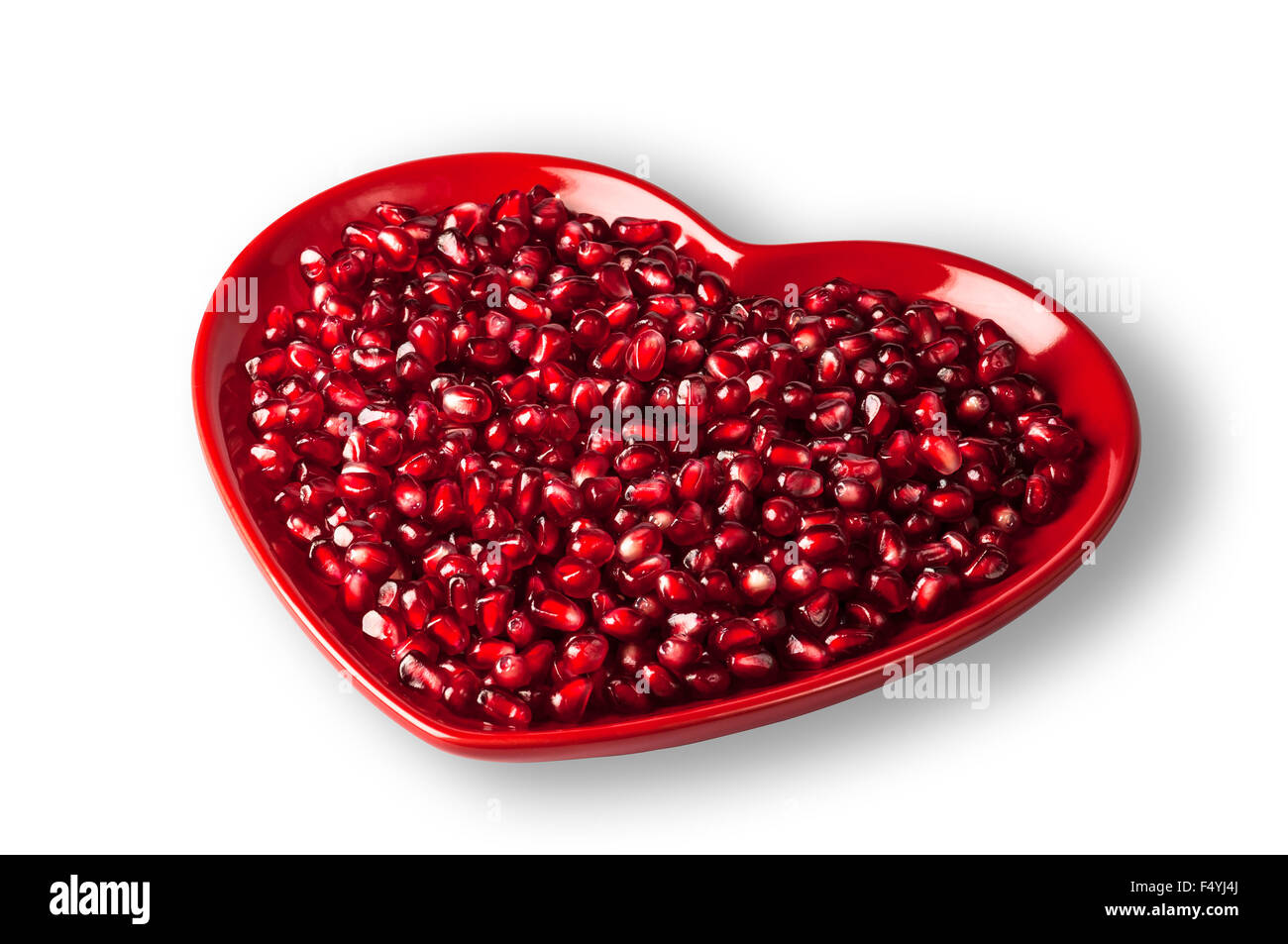 Red heart shaped plate full of delicious ripe juicy pomegranate seeds Stock Photo