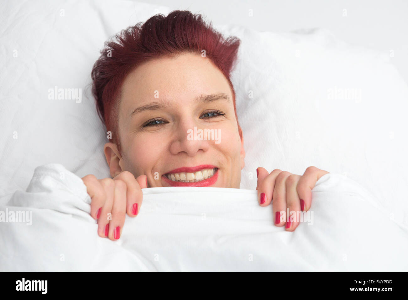 red-haired woman lying in bed on white pillow with a big smile Stock ...