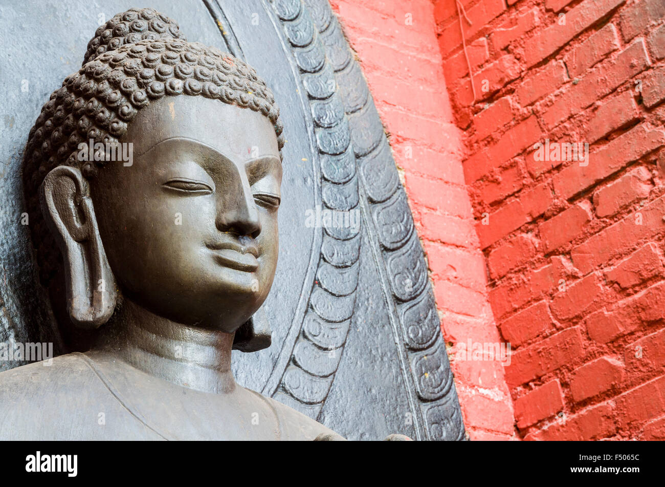 Head of a Buddha sculpture with red wall at Swayambhunath Stupa, the Monkey Temple Stock Photo