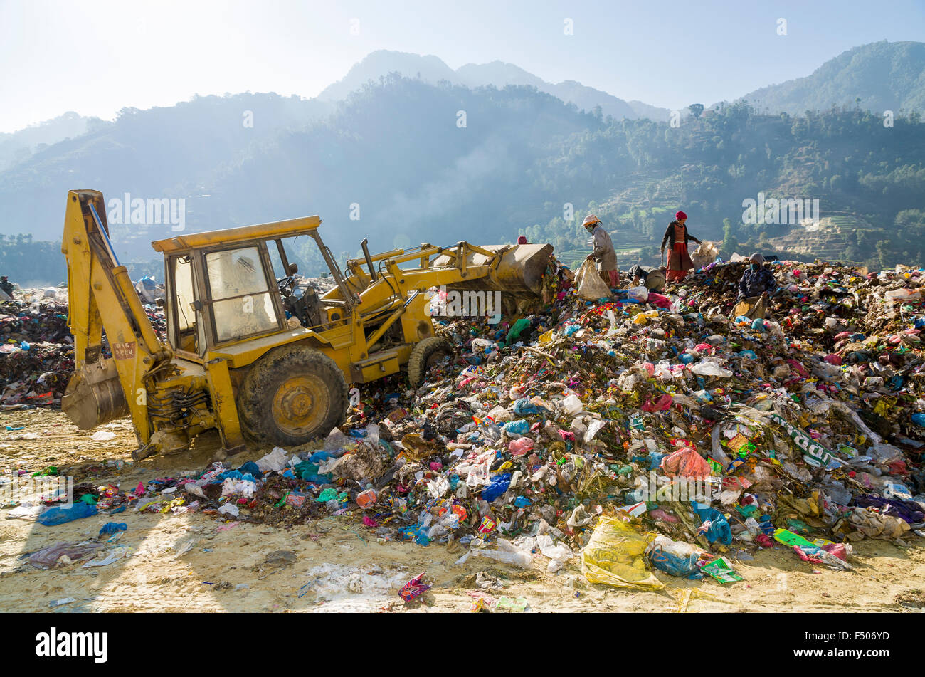 Bucket excavator shoving garbage to a heap, 2 workers beside, at Aletar garbage dump Stock Photo