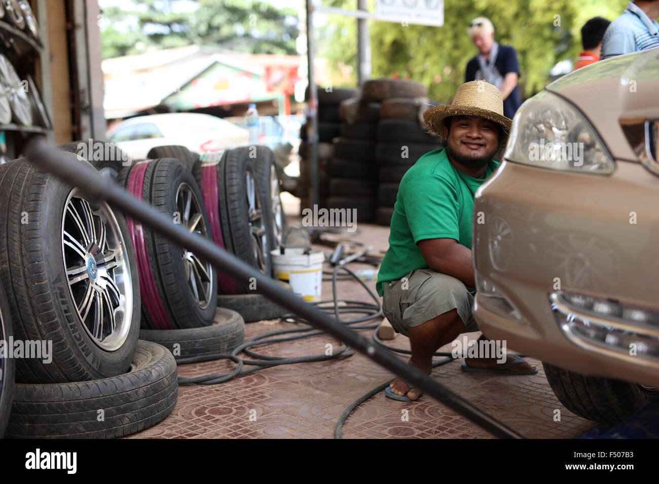 Man with straw hat and green shirt changing tire on golden car Stock Photo