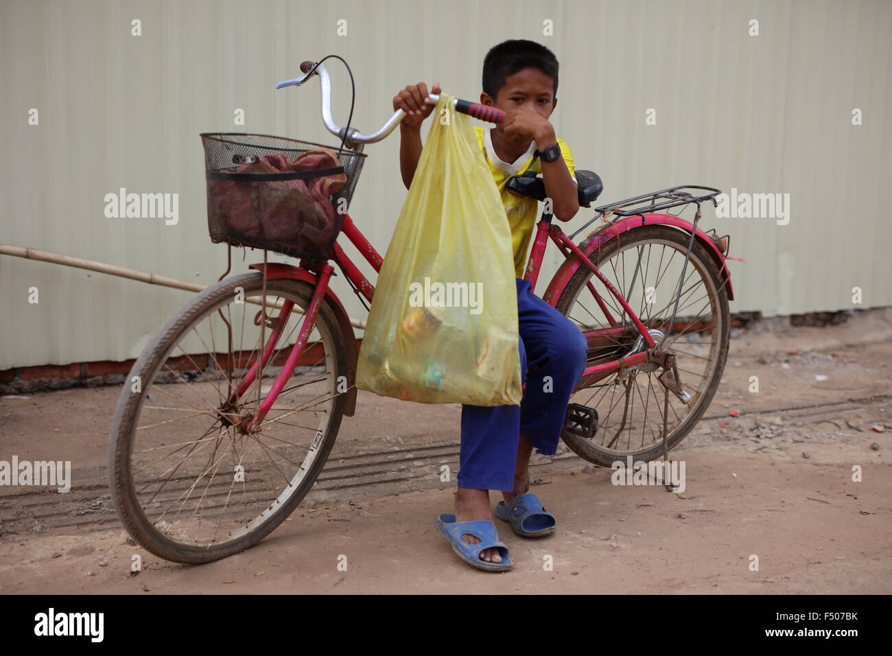 young boy sitting on his pink bicycle in Sisophon Cambodia holding his hand in front of his face. Stock Photo