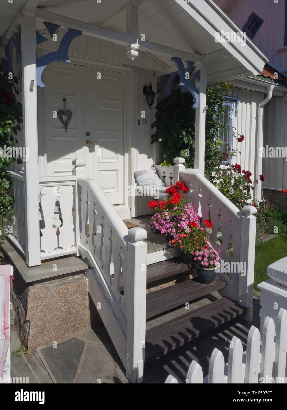 Old idyllic white wooden paneled house, front porch with bench, flowers