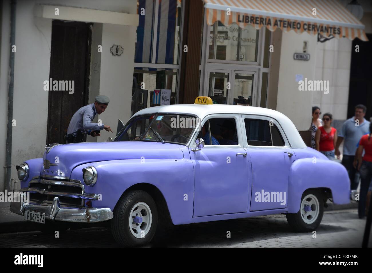 traffic cop speaking to taxi driver of a vintage mauve cab on a street corner in Havana Cuba Stock Photo
