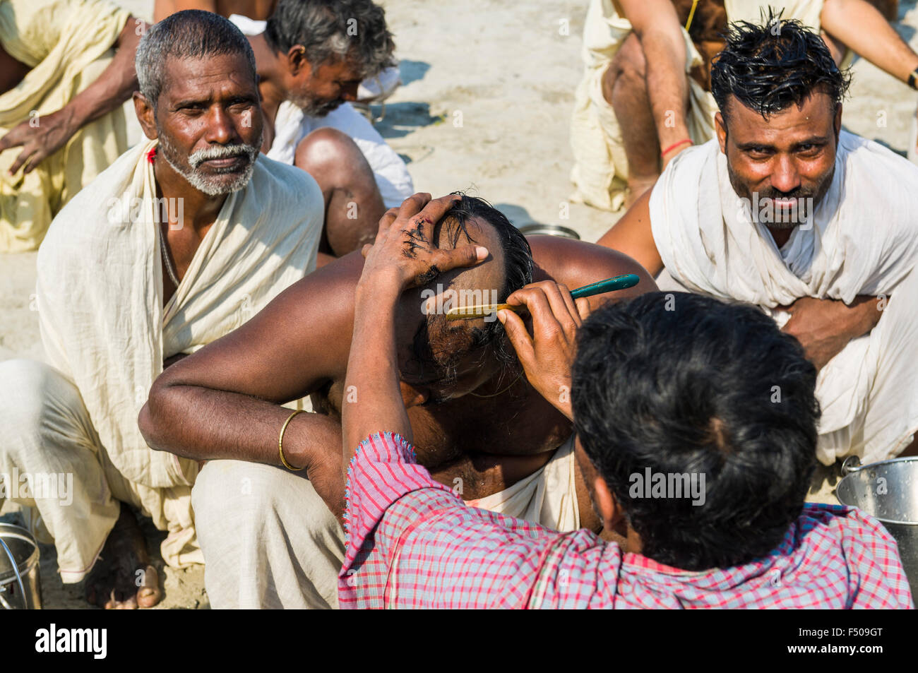 Group of male pilgrims getting their heads shaved at the Sangam, the confluence of the rivers Ganges, Yamuna and Saraswati, at K Stock Photo