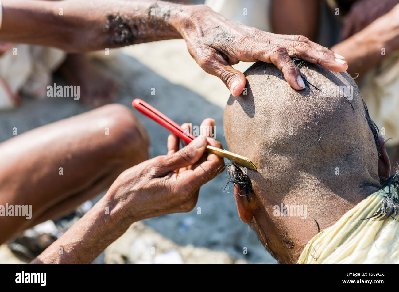 Pilgrim getting his head shaved at the Sangam, the confluence of the rivers Ganges, Yamuna and Saraswati, at Kumbha Mela Stock Photo