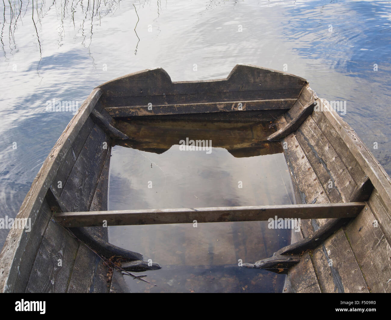 Old wooden rowing boat on the shore of  small Norwegian lake, weathered, worn waterlogged and in need of repair, sky reflections Stock Photo