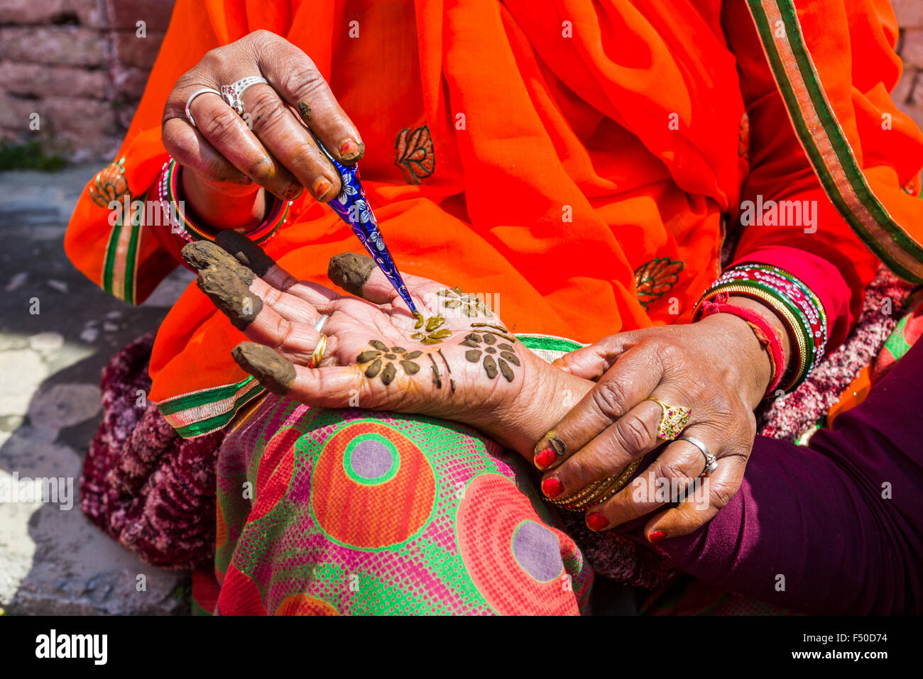 An indian woman is painting a hand with henna in front of the colorful Badrinath Temple, one of the Dschar Dham destinations Stock Photo