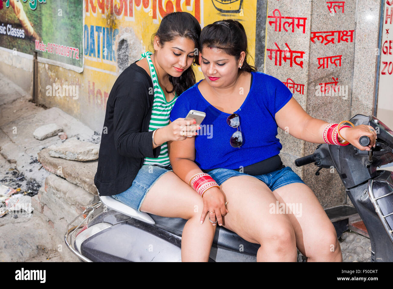 https://c8.alamy.com/comp/F50DKT/two-young-indian-women-in-shorts-are-sitting-on-a-scooter-and-using-F50DKT.jpg