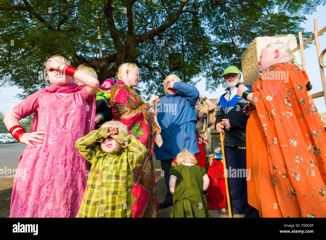 A family of Albinos, all have extremely pale skin and near-white hair, is standing on the street and covering their eyes from th Stock Photo