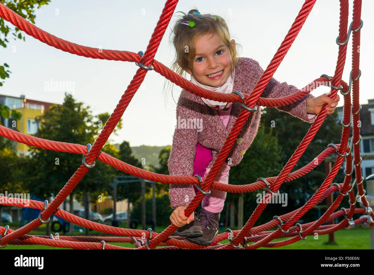 A three year old girl is climbing a rope scaffold Stock Photo