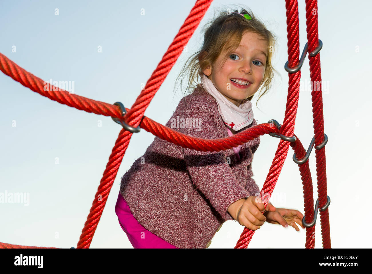 A three year old girl is climbing a rope scaffold Stock Photo