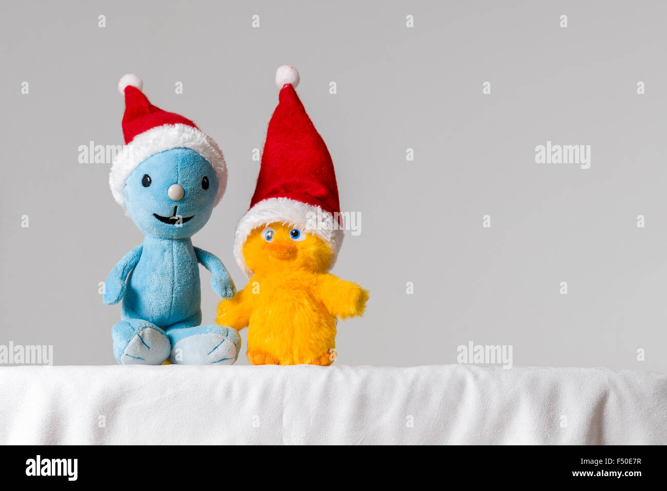 A light blue and a yellow cuddly toy, wearing Santa Claus hats, are sitting together on a white table Stock Photo