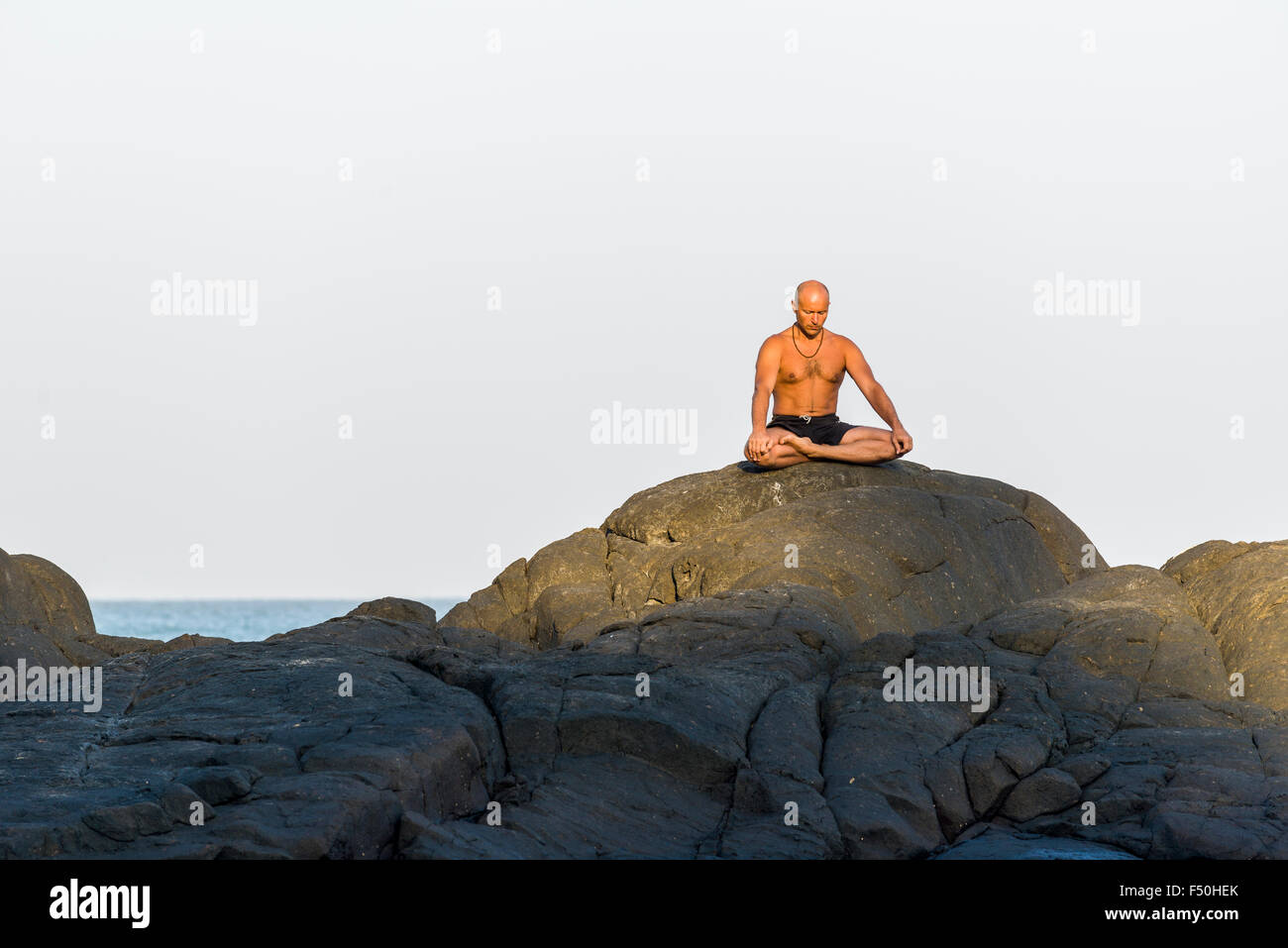 A man is meditating, practicing yoga on a rock at Kudle Beach, one of the famous beaches next to the temple town and pilgrimage Stock Photo