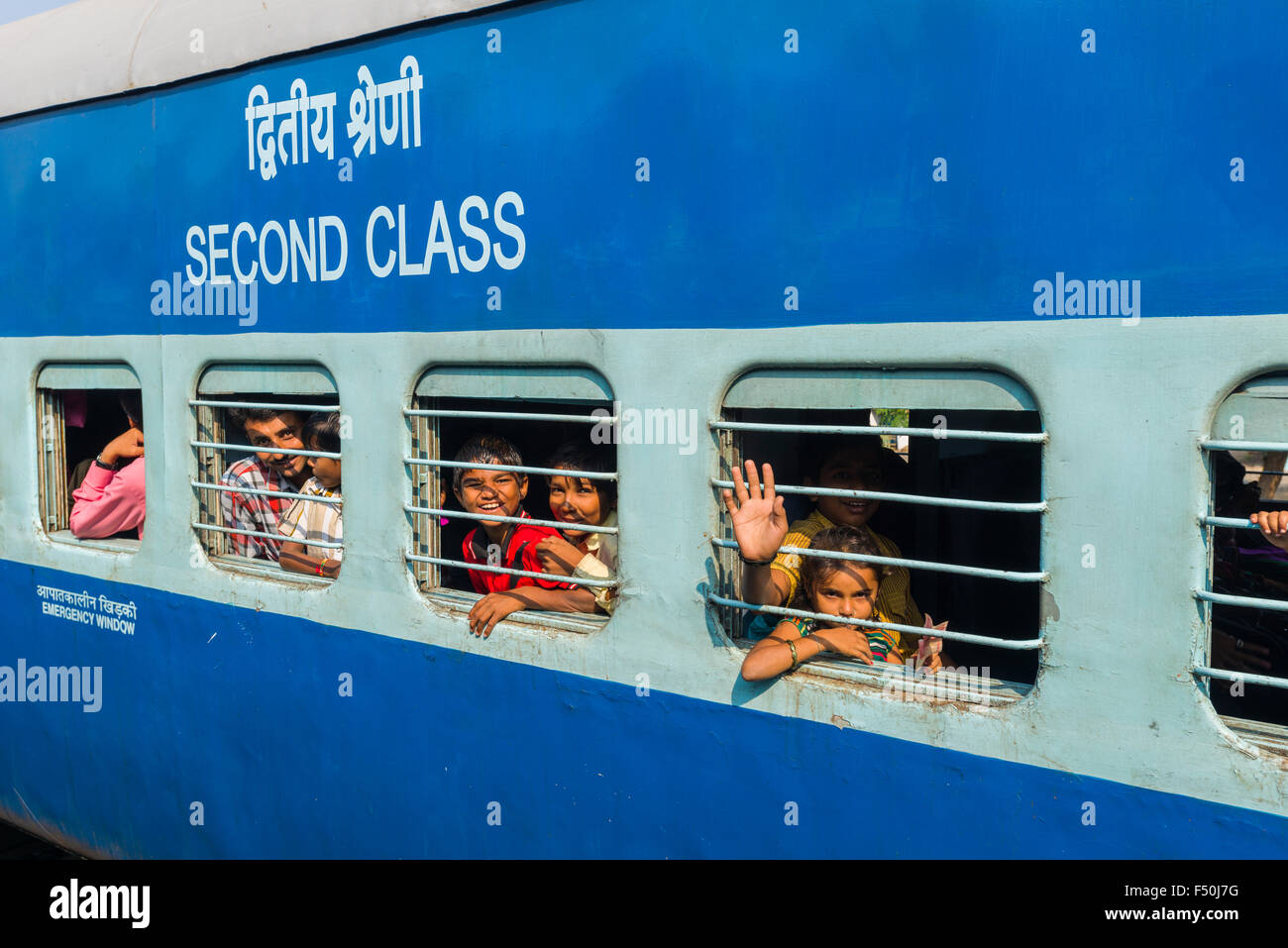 A blue colored train coach of Indian Railways with 'Second Class' written on it, passengers are looking out of the windows behin Stock Photo