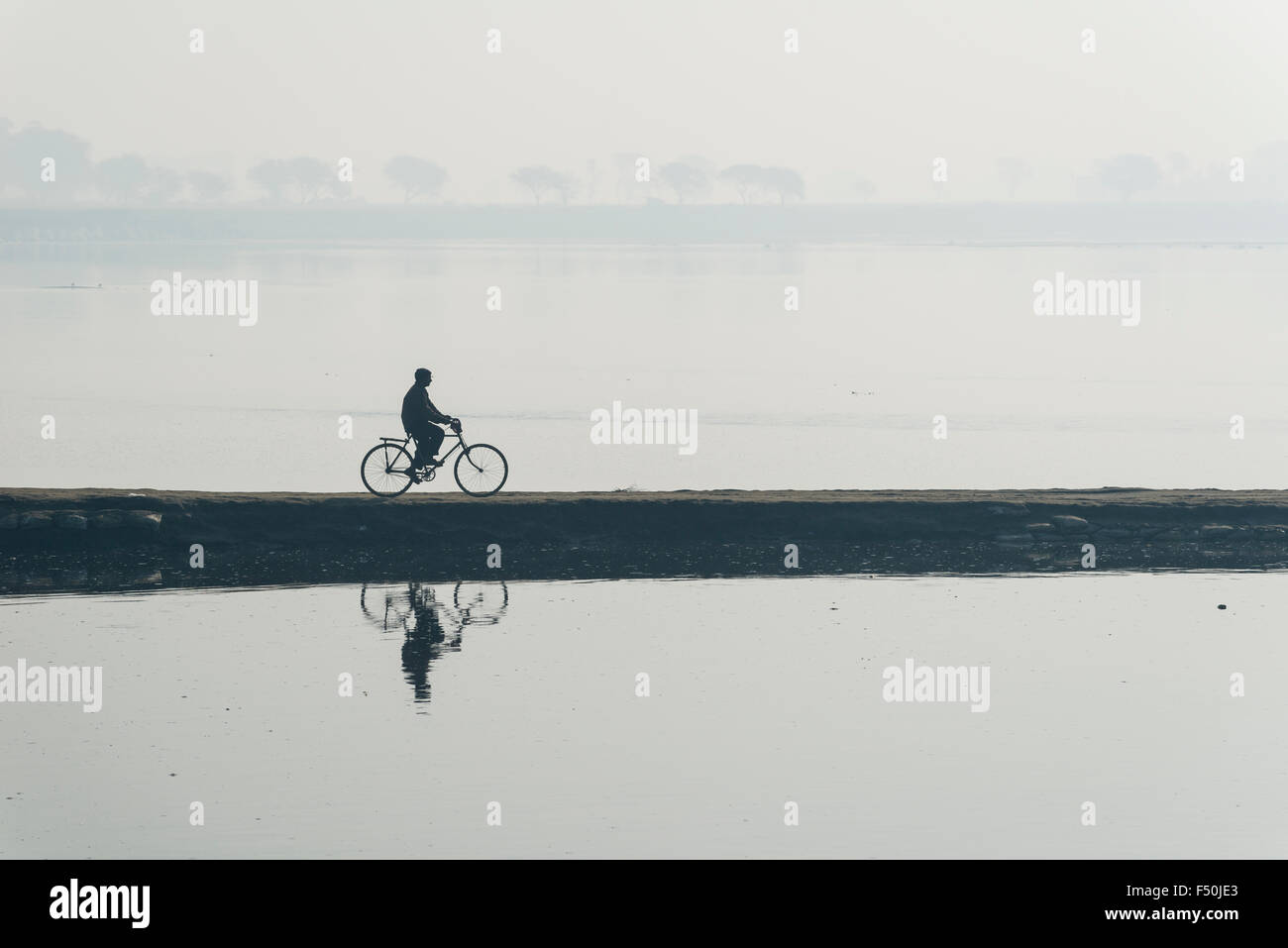 A cyclist is crossing the Yamuna river on a dam in the morning haze Stock Photo