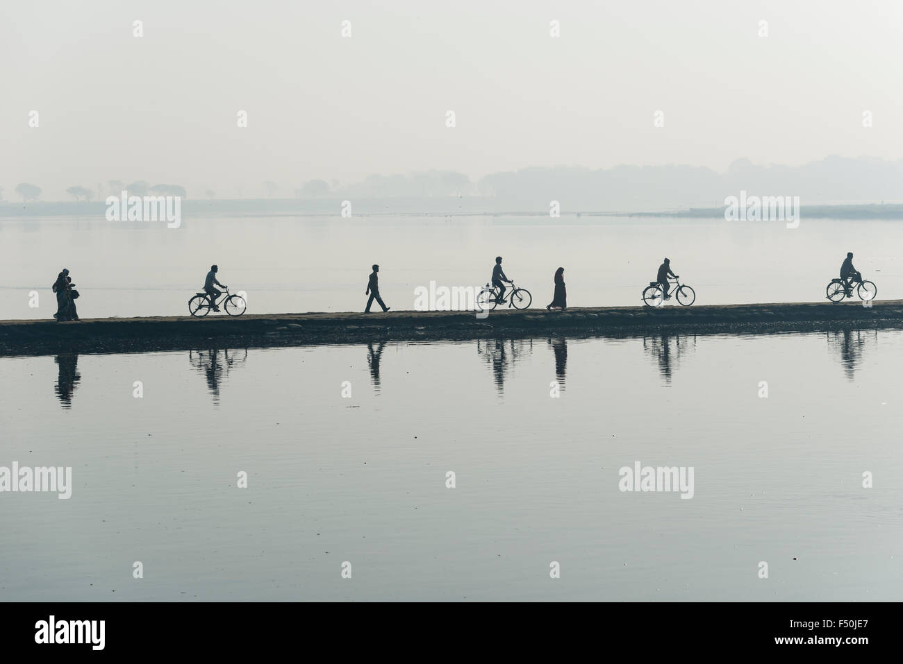Some cyclists and pedestrians are crossing the Yamuna river on a dam in the morning haze Stock Photo