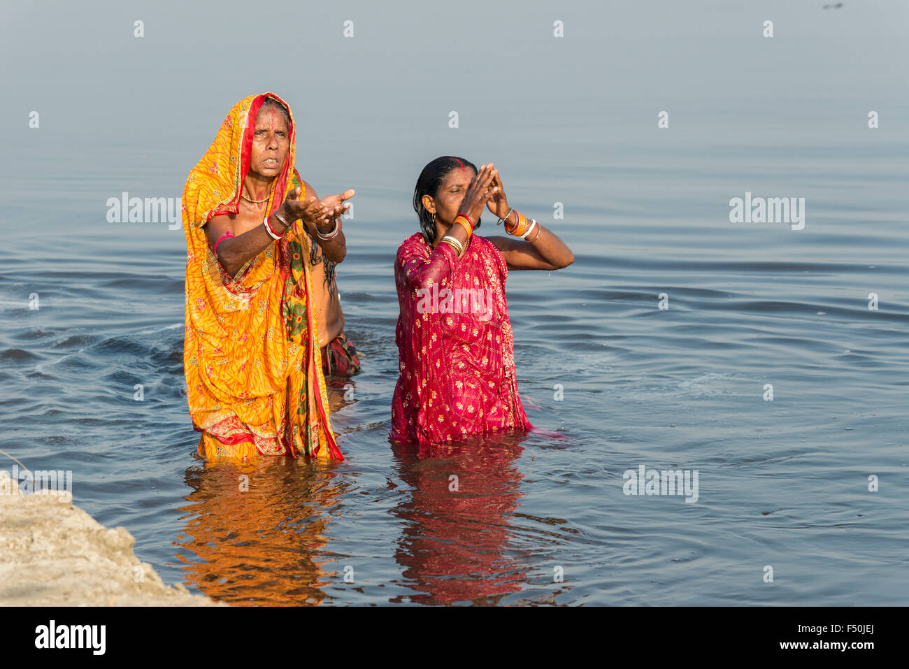 Two female pilgrims, women, are taking bath and praying in the holy river Yamuna Stock Photo