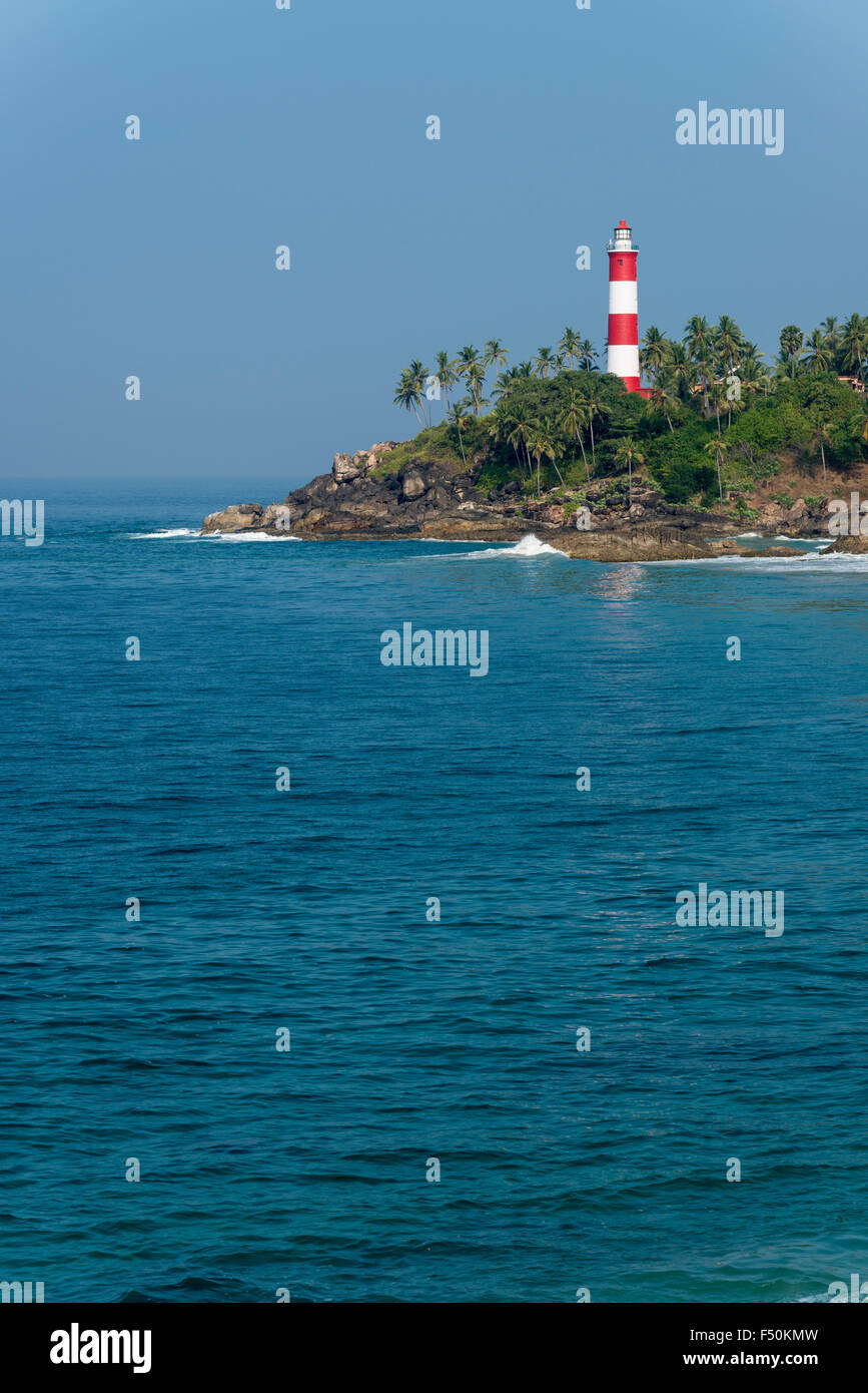 The light house at Kovalam Beach is located on a small peninsula with palmtrees and surrounded by blue water Stock Photo