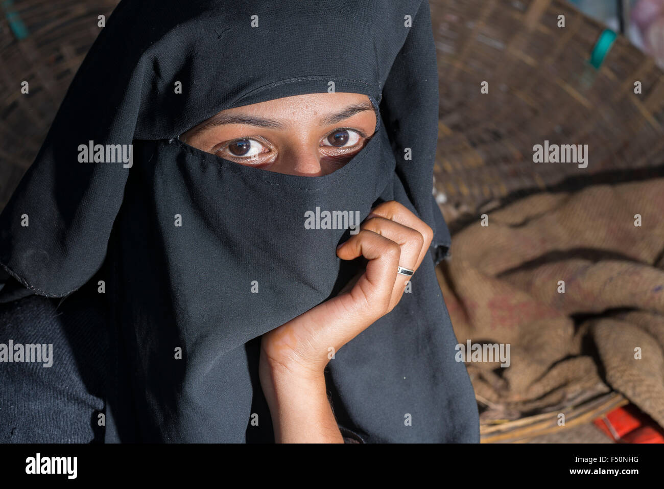 A young muslim woman, her face covered by a black hijab, veil, is selling vegetables in the market Stock Photo