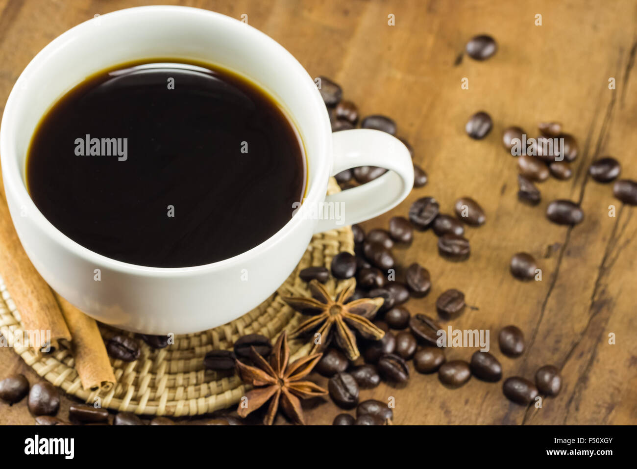 coffee on the cup with coffee beans and cinnamon sticks on wood background, warm toning, selective focus Stock Photo