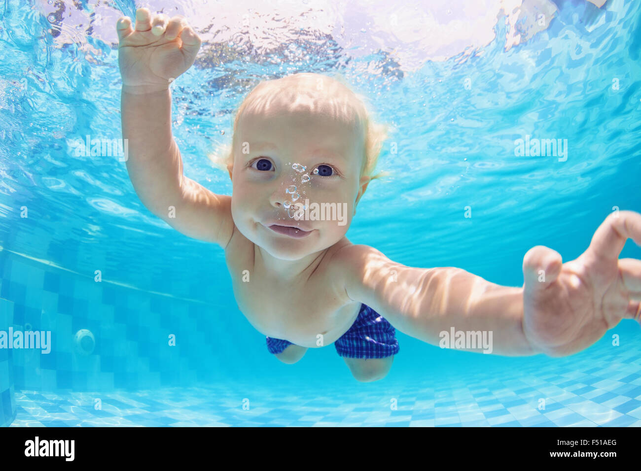 Funny face portrait of little baby boy having a water exercises - swimming and diving underwater with fun in the blue pool. Stock Photo